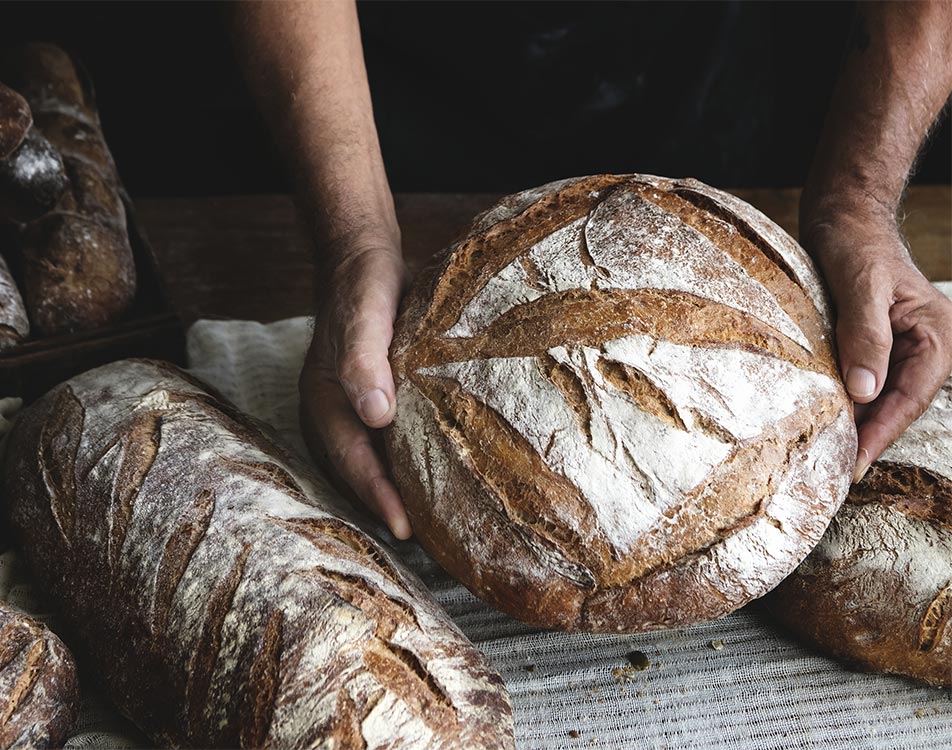 Pain rond entre deux mains à côté d'un pain artisanal